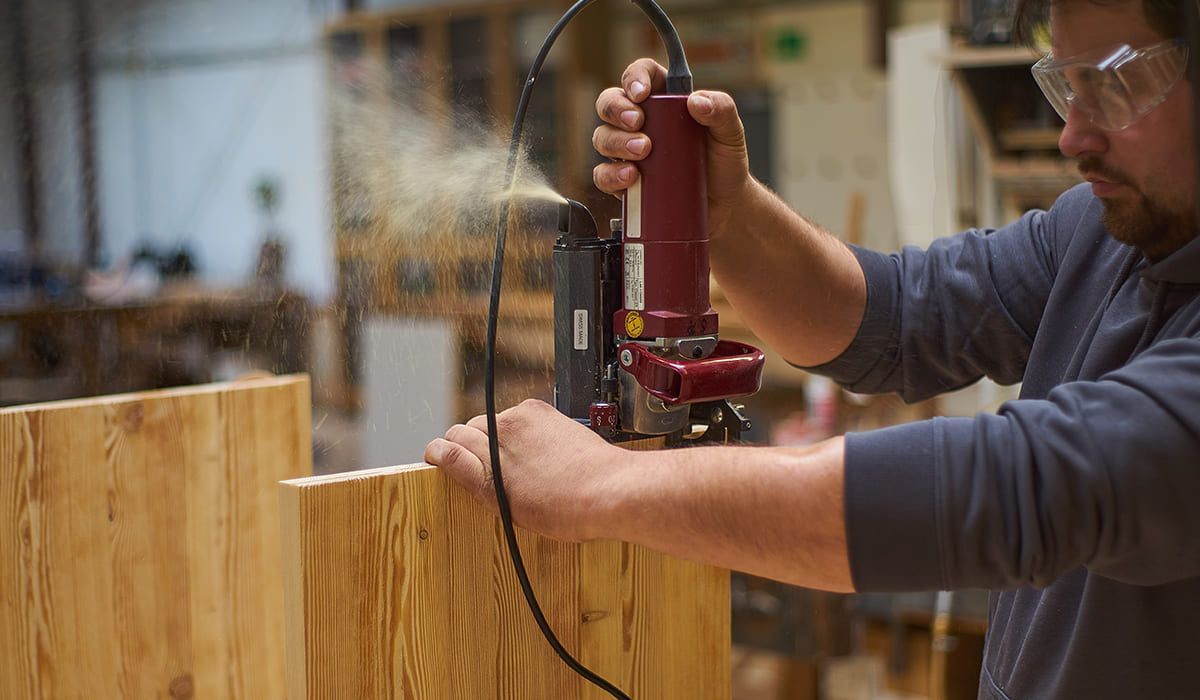 Ein Mann benutzt eine Bohrmaschine, um Holz zu schneiden, während er konzentriert auf seine Arbeit schaut.